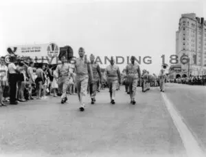 Black and white photo of men in uniform marching down the street.