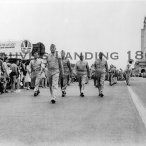 Black and white photo of men in uniform marching down the street.